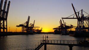 Container terminal in the harbor of Hamburg, Germany, with cargo cranes at sunset.