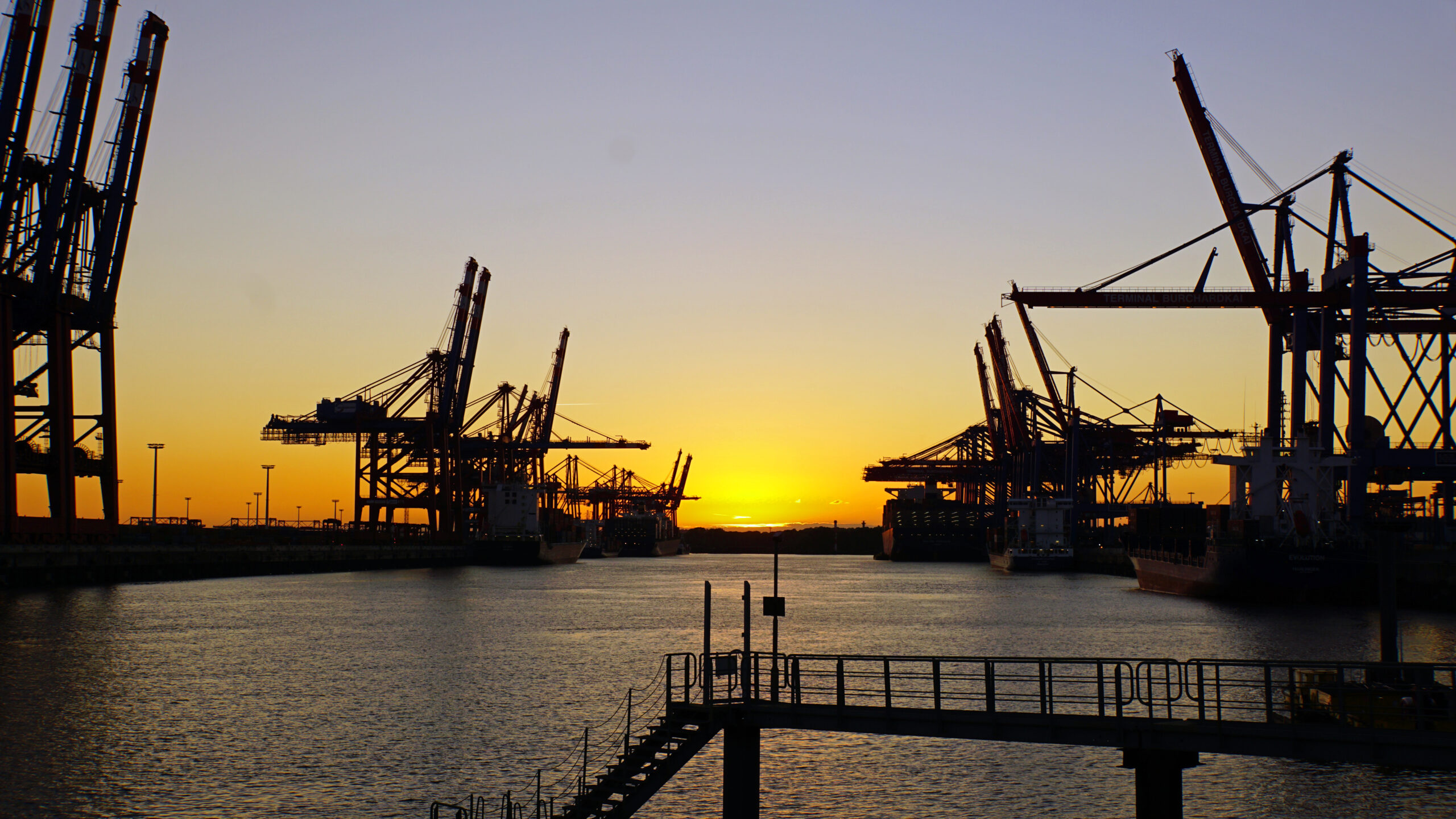 Container terminal in the harbor of Hamburg, Germany, with cargo cranes at sunset.